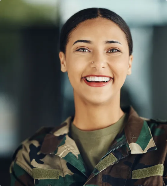Portrait of a smiling woman in camouflage military uniform with dark hair pulled back.