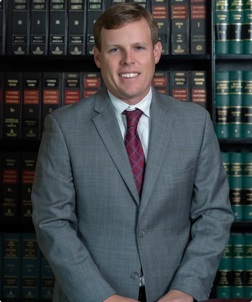 Professional man in gray suit and red tie standing in front of law bookshelves.