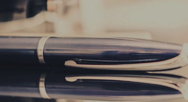 Close-up of a sleek black and silver pen resting on a reflective dark surface.